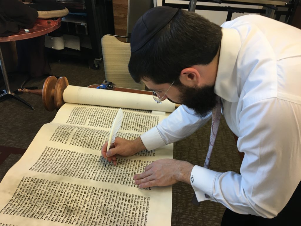 photo: Before going to Poland the Torah was checked and damaged letters were repaired. Scribe Menachem Bialo is seen here fixing the Torah.